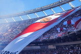 Large red and white flag with text held by a crowd at a stadium
