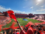 A view from the terrace from theIndependiente stadium with fans waving red flags and smoke, blue sky above
