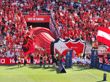 Soccer stadium with fans in red shirts and a large inflatable palyer's tunnel in the form of a shield emblem on the field