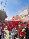 Group of Independiente fans in red and white clothing on a street, with a clear blue sky.