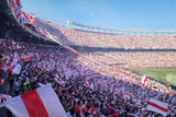 Large sports stadium filled with spectators waving red and white flags on a clear day.