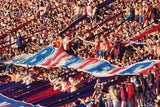 Fans in a stadium with large flags, cheering and waving. San Lorenzo Stadium.