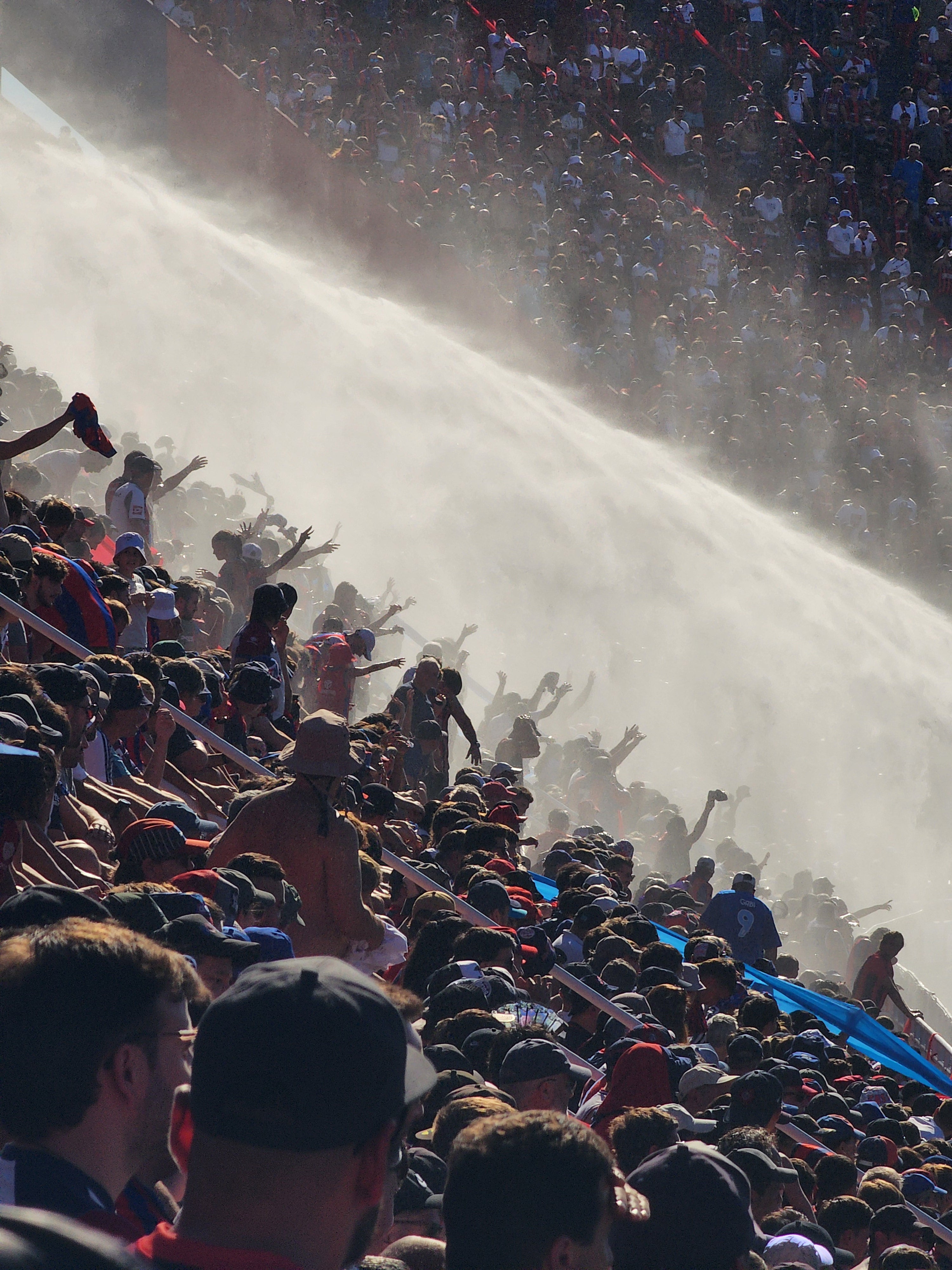 San Lorenzo de Almagro fans in the terraces of the Nuevo Gasómetero stadium on a hot day being sprayed with water from a firefighter's hose